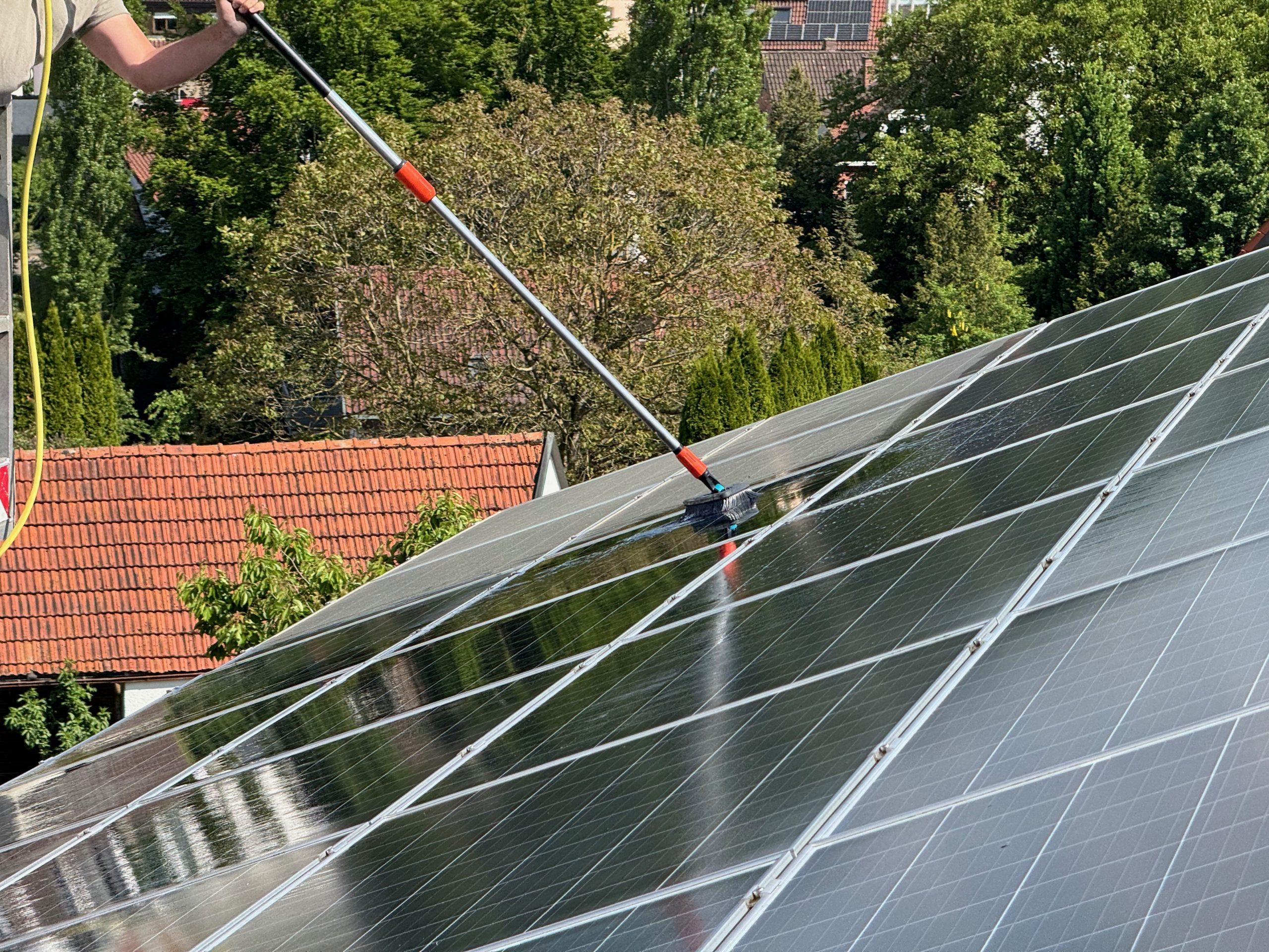 PV Paneele auf einem Hausdach, die vor Projektabschluss noch gewaschen werden mit einer professionellen Bürste, die auch einen Wasserauslass hat